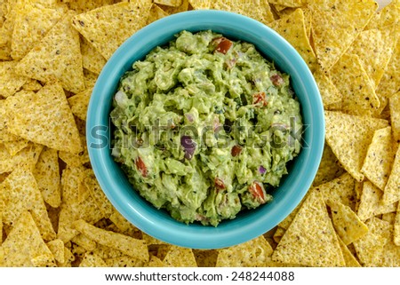 Homemade chunky guacamole in bright blue bowl surrounded by yellow corn tortilla chips