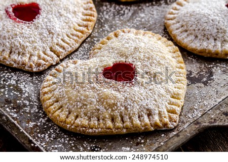Close up of heart shaped cherry hand pies dusted with powdered sugar sitting on metal baking pan