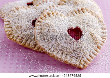 Close up of heart shaped cherry hand pies dusted with powdered sugar sitting on pink polka dot background
