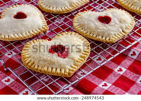 Heart shaped cherry hand pies sitting on wire cooling rack on top of red and white heart kitchen towel