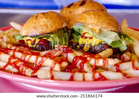 Plate of three hamburger sliders sitting on plate with french fries topped with ketchup on bar top
