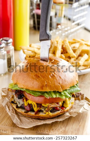 Close up of gourmet pub hamburger with bacon on wooden cutting board with plate of french fries sitting on wooden table