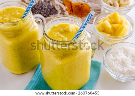 Close up of fresh blended fruit smoothies made with pineapple, banana, coconut, turmeric and chia seeds surrounded by raw ingredients with blue straws