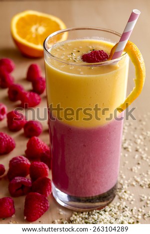 Fresh blended fruit smoothie made with mango, orange, cantaloupe, raspberries, strawberries and hemp seeds surrounded by raw ingredients with pink swirled straw