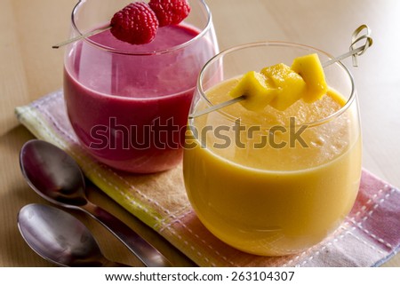 Close up of 2 fresh blended fruit smoothies made with mango, orange, cantaloupe, raspberries, and strawberries garnished with fruit pieces