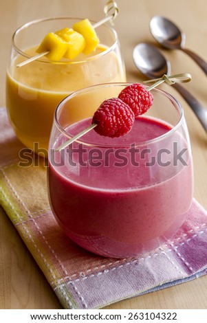 2 fresh blended fruit smoothies made with mango, orange, cantaloupe, raspberries, and strawberries garnished with fruit pieces