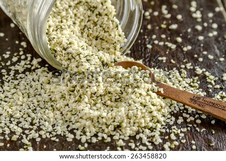 Organic hemp seeds spilling out of glass jar with measuring spoon on wooden table