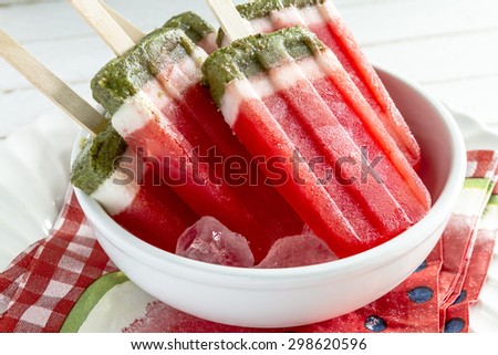 Close up of frozen fresh fruit watermelon and kiwi popsicles in white bowl with ice cubes sitting on watermelon napkins