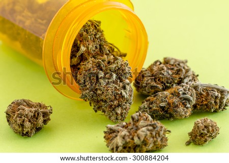Medical marijuana buds spilling out of prescription bottle on green background