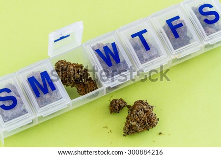 Medical marijuana buds in daily pill organizer sitting on green background