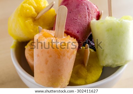Assorted flavors of homemade fresh pureed frozen fruit popsicles sitting on white bowl on wood table
