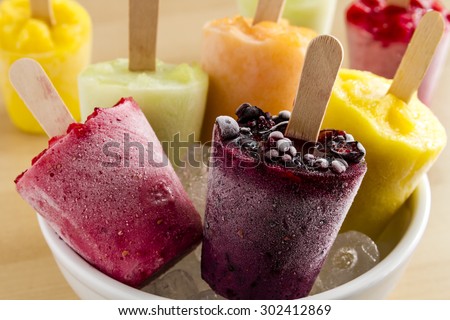 Close up of assorted flavors of homemade fresh pureed frozen fruit popsicles in white bowl with ice
