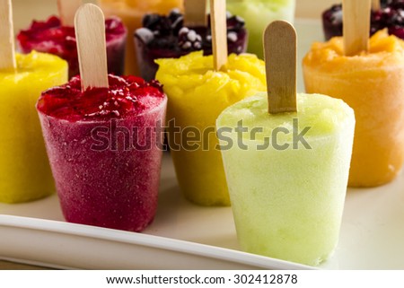 Assorted flavors of homemade fresh pureed frozen fruit popsicles on white plate