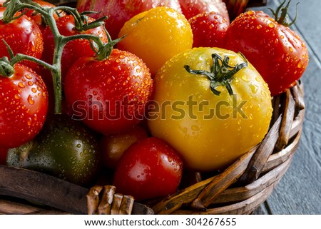 Assortment of colorful heirloom tomatoes with water drops in dark wooden basket