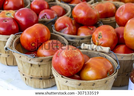 Fresh organic red tomatoes in brown bushel baskets sitting on table at local farmers market