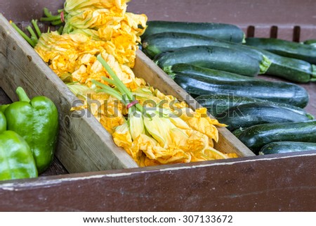 Box filled with pumpkin blossoms, green peppers and green zucchini squash for sale at local farmers market