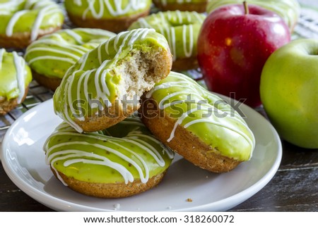 Plate of homemade baked caramel apple donuts with green apple glaze with bite out of top donut sitting on white plate with fresh apples in background