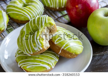 Plate of homemade baked caramel apple donuts with green apple glaze with bite out of top donut sitting on white plate with fresh apples in background