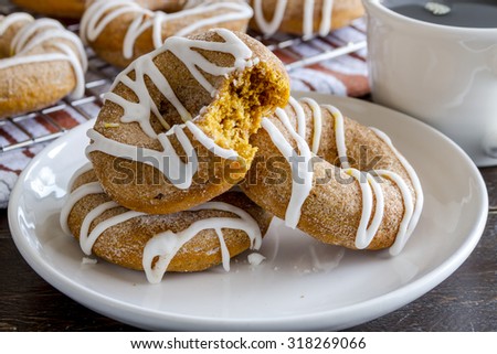 3 homemade cinnamon pumpkin donuts on white plate with bite taken out of one donut with cup of coffee