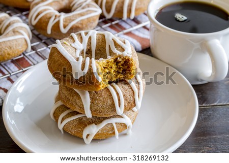 Stack of three homemade cinnamon pumpkin donuts on white plate with bite taken out of top donut with cup of coffee