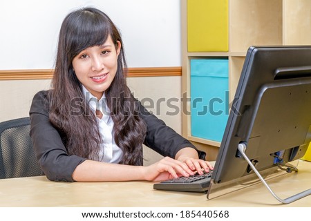 Asian female secretary typing at desk smiling