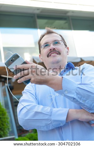 Urban man using smart phone outside using app on 4g wireless device wearing headphones. Adult urban professional male in his late 40s.