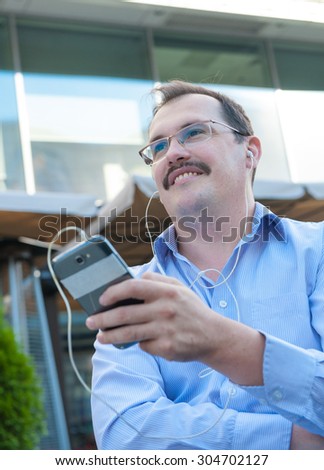 Urban man using smart phone outside using app on 4g wireless device wearing headphones. Adult urban professional male in his late 40s.
