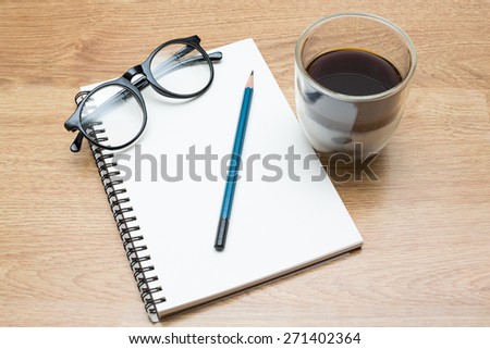 A coffee and cup  and a book, pencil, glasses on the wood table