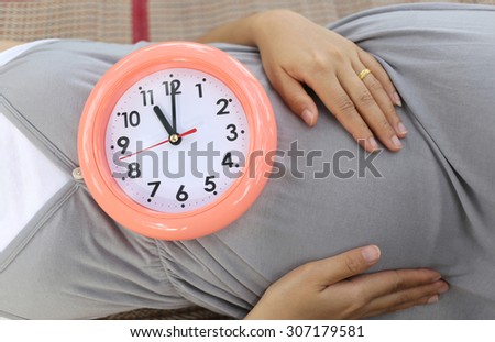 Pregnant women show clock on her belly to tell the time Eleven o\'clock.