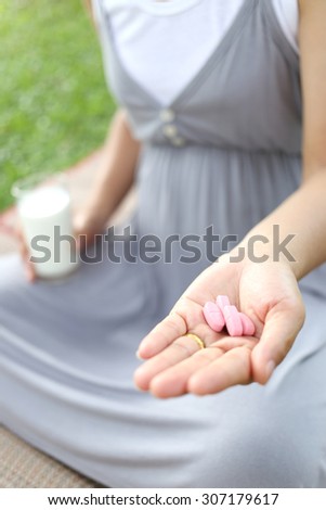 Pregnant women have a glass of Milk and vitamin pill in hand to eat for health of the baby.