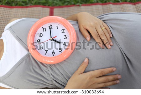 Pregnant women show clock on her belly to tell the time four o\'clock.