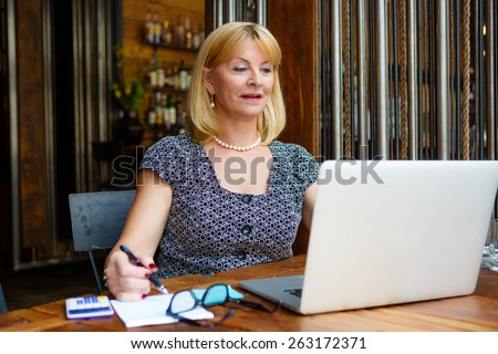 Smiling old senior blonde business woman 60-65 years, alone with laptop in summer cafe
