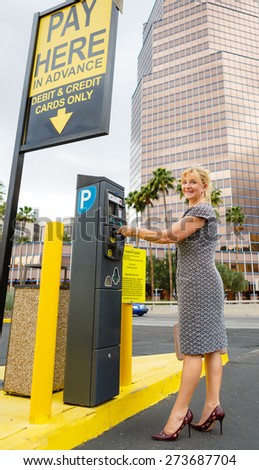Trendy attractive senior aged business woman 55-65 years with a lovely charming smile paying for parking in the street. Positive human emotion, facial expression
