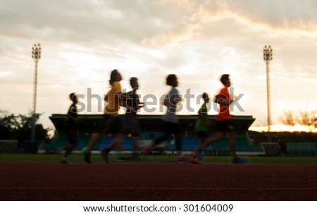 group running on race track on soccer stadium, sunset