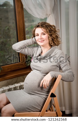 Pregnant woman drinking milk in the room sitting on a chair, Happy pregnant woman drinking milk