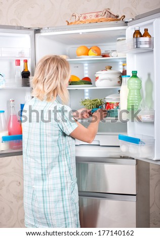 Young beautiful girl takes food from the refrigerator. Storing food in the refrigerator