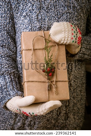Hands in mittens holding gift box. Christmas gift wrapped in brown paper and twine held in hands with mittens