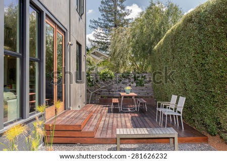 Modern home with large windows and amazing outside terrace with table and chairs. Green house with deck and zen garden.