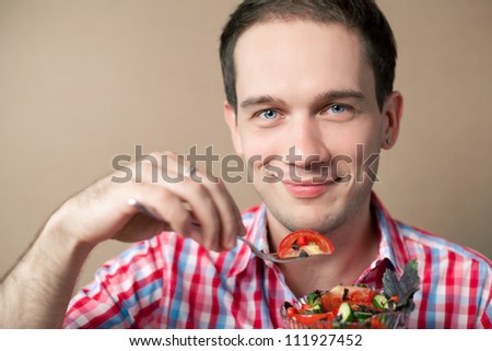 Close-up portrait of a slim handsome boy eating salad over wooden background. studio shot