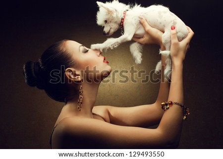 Portrait of two playing friends:  fashionable model with sexy red lips holding her white little chinese crested dog. Both posing over golden background. Studio shot