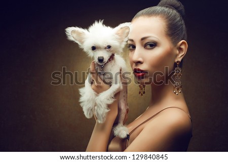 Portrait of two friends:  fashionable model with sexy red lips holding her white little chinese crested dog. Both posing over golden background. Copy-space. Studio shot