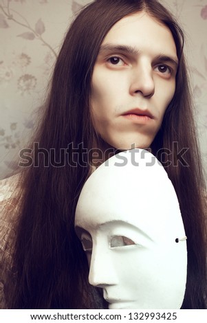 Portrait of a handsome long-haired poet with a white italian (venetian) mask volto bianco waiting for inspiration. Vintage (classic) style. Studio shot.