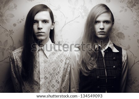 Portrait of beautiful long haired people in vintage style: handsome boy with black hair and gorgeous blonde girl posing together. Black and white (monochrome) studio shot.