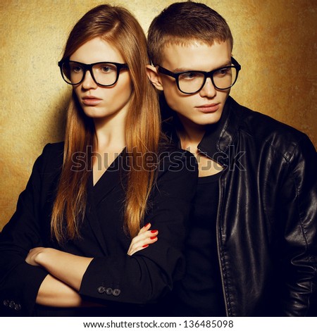 Portrait of gorgeous red-haired fashion twins in black clothes wearing trendy glasses and posing over golden background together. Perfect hair. Natural make-up. Perfect skin. Studio shot.