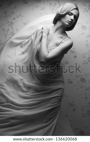 Vintage portrait of a happy glamorous blonde girl posing in great flying white dress and dancing. Retro (classic) style. Black and white (monochrome) studio shot