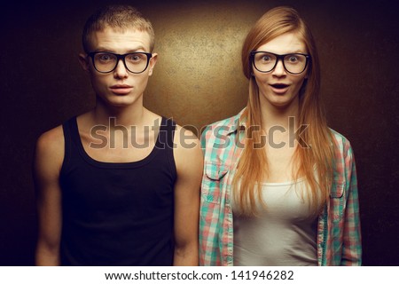 Portrait of gorgeous red-haired (ginger) fashion twins in casual shirts wearing trendy glasses and posing over golden background together with wow faces (duck-face). Hipster style. Studio shot
