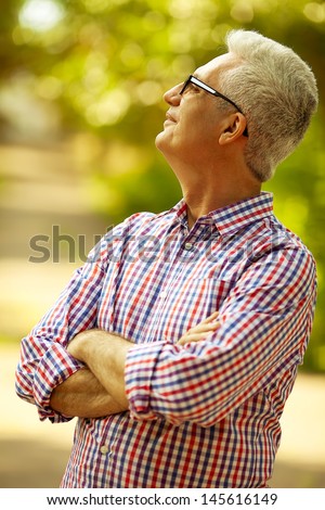 Successful man concept. Portrait of a smiling happy mature (old) man in trendy casual shirt & stylish glasses looking up and posing in the park. Sunny summer day. Copy-space. Outdoor shot
