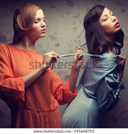 Seduction (forbidden love) concept. Retro portrait of two gorgeous young women (girlfriends) in blue and orange dresses in a hotel room. Vintage (old hollywood) style. Studio shot