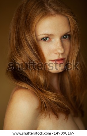 Portrait of a smiling beautiful red-haired (ginger) girl with funny freckles on her face posing over wooden background. Healthy long and wavy hair. Daylight. Close up. Studio shot