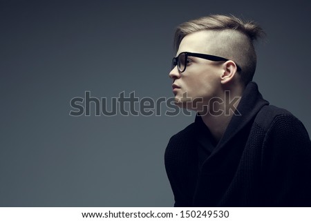 Male beauty concept. Portrait of fashionable young man with stylish haircut wearing trendy glasses and sweater, posing over gray background. Perfect hair & skin. Hipster style. Copy-space. Studio shot